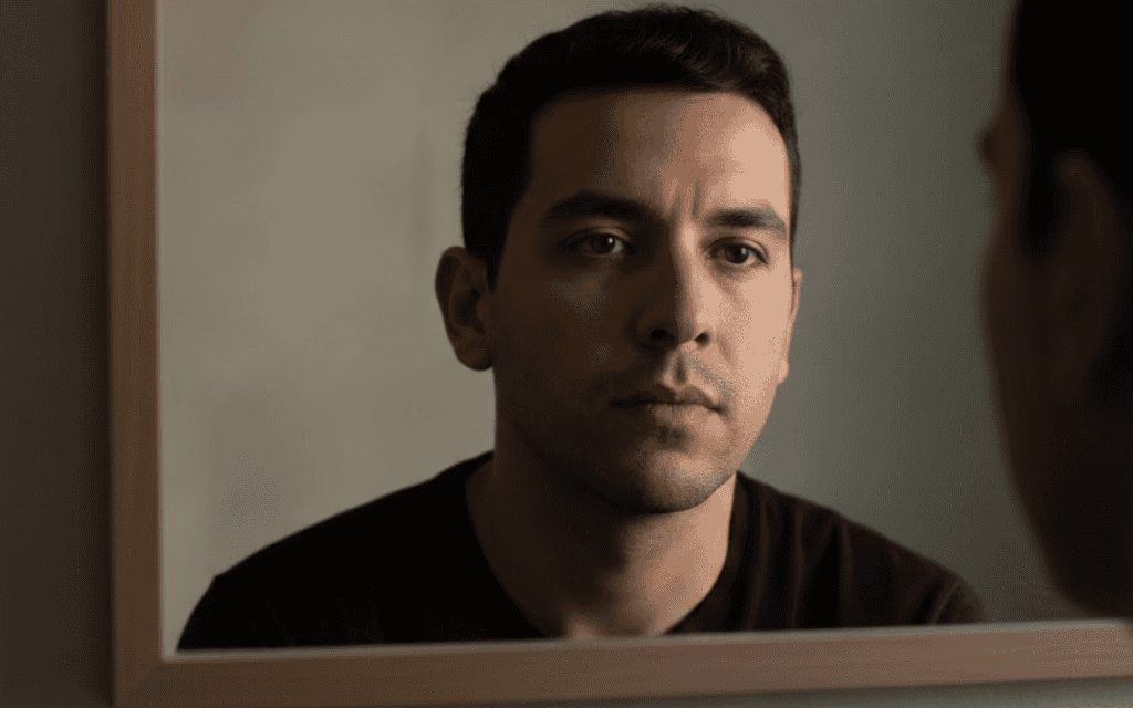 A man wearing a black shirt, staring into a mirror.